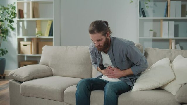 Man sitting on the couch suddenly felt pain in his stomach. Man trying to relieve pain by massaging his stomach