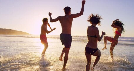 Beach, sunset and people playing in ocean together for fun on travel, vacation or holiday in summer. Splash, wave and group of young friends in sea or water outdoor on tropical coast for getaway - Powered by Adobe