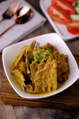 Tengkleng Kambing is a traditional Central Javanese dish made from young goat bones, with spices, soy sauce, chili. served in a white ceramic bowl on a brown wooden table. Indonesian food. 