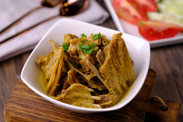 Tengkleng Kambing is a traditional Central Javanese dish made from young goat bones, with spices, soy sauce, chili. served in a white ceramic bowl on a brown wooden table. Indonesian food. 