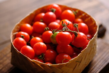 fresh cherry tomatoes in a bamboo basket on a brown wooden rustic table. Contains vitamins C, A, lycopene. Solanum lycopersicum var. cerasiforme. Cherry tomato. Tomat Ceri. 
