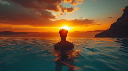 Papier Peint photo autocollant Europe méditerranéenne man relaxing in the infinity swimming pool looking at the ocean at sunset, a young man in the swimming pool relaxing looking out over the ocean caldera of Oia Santorini Greece on a sunny day