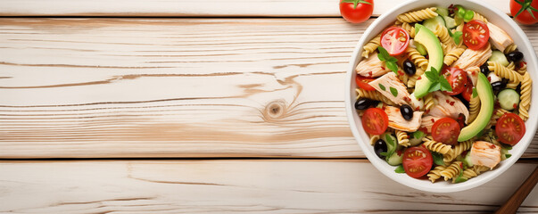 From above, a white bowl holds a delicious Chicken Pasta Salad adorned with avocado, tomato, and dressed with olive oil and vinegar on a white wood table. A visually appealing image, ideal for creativ - obrazy, fototapety, plakaty