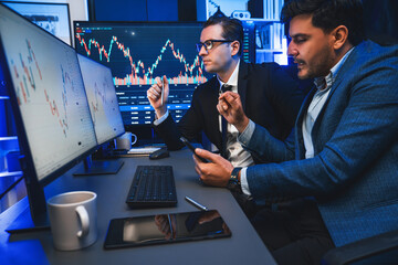 Two stock exchange traders discussing dynamic investment graph in currency rate on monitor at...