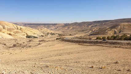 Scenic panoramic view of mountainous desert terrain with wind turbine farm in distance in Jordan,...