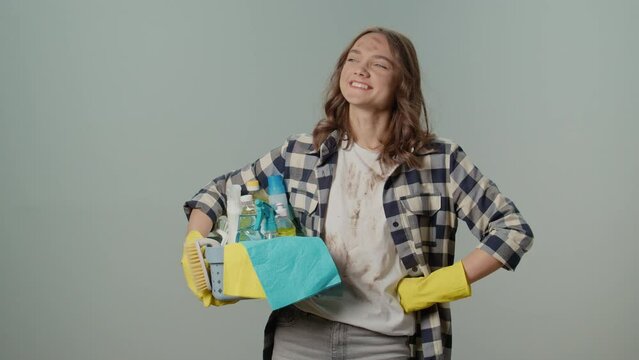 A Smiling Dirty Young Woman in Yellow Protective Rubber Gloves, Holding a Box With Cleaning Products, Satisfied with the Result of Her Cleaning, on the Gray Background.Pet-friendly Cleaning Solutions.