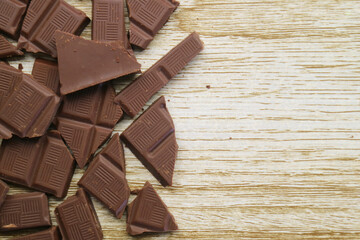 Heap of cracked dark chocolate bars scattered on wooden background