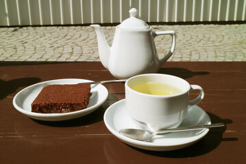 Cup of hot tea with a slice of brownie and teapot on the sunny garden table