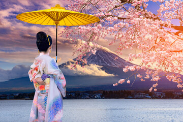 Asian women wear Japanese kimonos. Holding a yellow umbrella at Mount Fuji and cherry blossoms at Lake Kawaguchiko in Japan. - 732224010