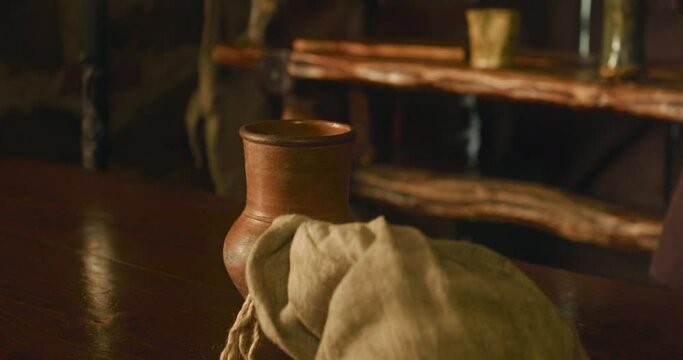 Knight puts sack on counter in roadside tavern closeup. Brave traveller in metal armour gives bag of artefacts to store owner at wooden desk. Medieval strategy