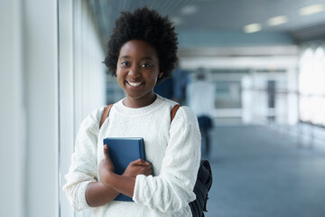 African girl, portrait and hallway of college with smile from happiness of education in academy. Student, learning and notebook on hand with information for class in school campus and scholarship