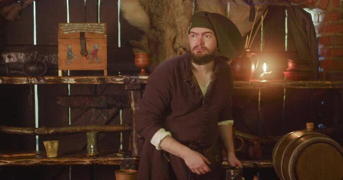 Nervous barkeeper looks at coming guest suspicious in inn. Worried innkeeper turns to counter in medieval tavern. Bearded dwarf sees noble visitor in pub