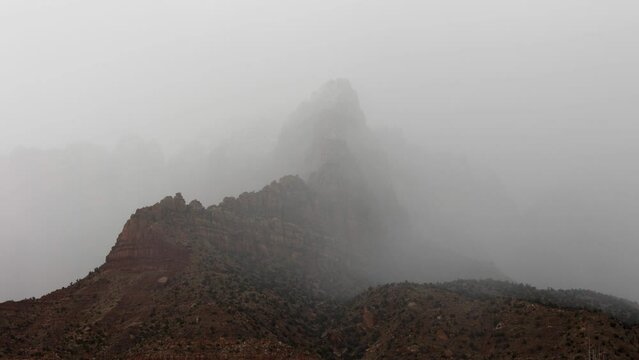 4k time lapse of low winter clouds swirling around the peak of Mt. Kinesava in Zion Nat. Park, Utah, USA on a chilly wet day. A patch of sunshine briefly lights the cliffs before more clouds move in.