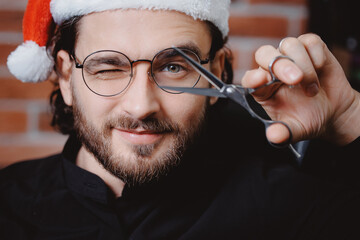Portrait happy barber man in christmas red hat, hairdresser hold scissors, barbershop xmas holiday