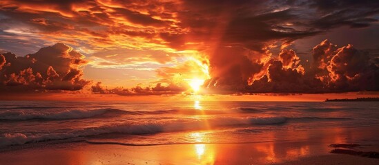 The sky is painted in amber and orange hues as the sun sets over the ocean, while waves crash onto the beach creating a serene natural landscape.