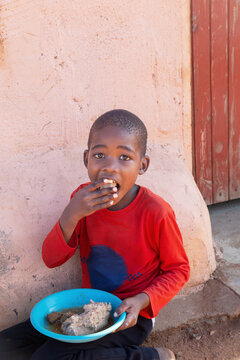 hungry village african child in the yard , sited on the ground eating staple bogobe slap pap and meat from plastic plates with their hands