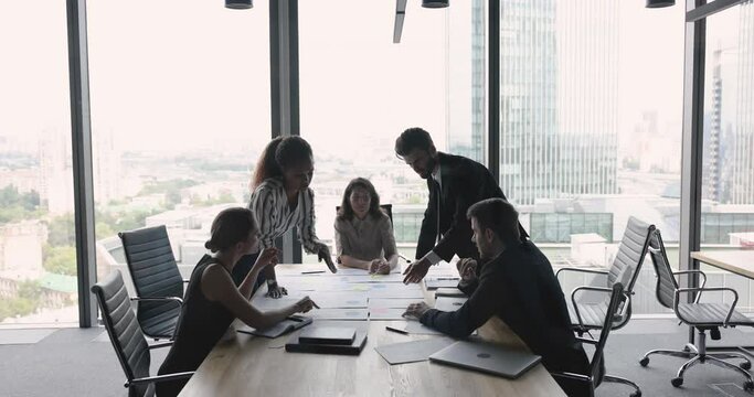 Diverse business colleagues talking on paper reports, bending over meeting table, pointing at diagrams in statistic documents, discussing marketing strategy, sales, project plan, management