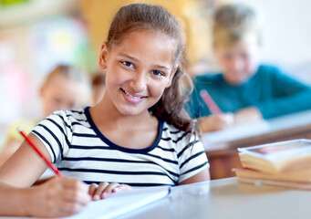 Child, portrait and school desk in class with notebook for lesson studying in academy or education, learning or knowledge. Female person, pupil and pencil with smile for writing test, exam or project