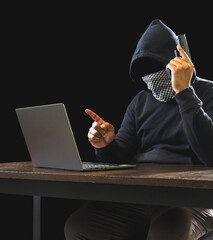 Portrait hacker spy man one person in black hoodie sitting on table looking computer laptop used...