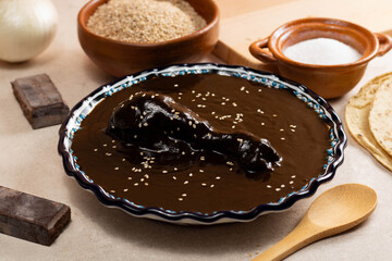 Talavera and clay dish filled with black mole, accompanied by tortillas and sesame seeds, on a cement background in Oaxaca
