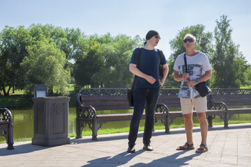 Men of two generations in informal clothes are having a conversation in a city park on a summer day