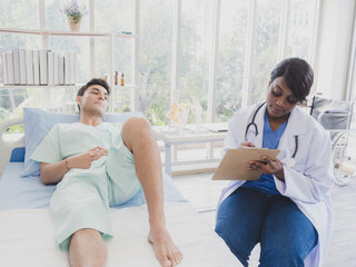 Portrait patient caucasian man with woman nurse carer physical therapist African-American two people sitting talk helping support give advice and holding relax check on leg body inside hospital