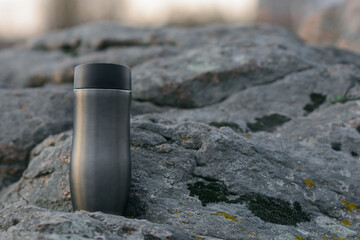 Tourist thermos mug on the background of mountains, stones and a river in which the sunset and clouds are reflected.