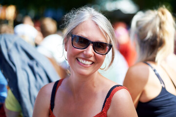 Senior, woman and portrait with sunglasses outdoor in crowd, happy and festival on vacation for fun. Person, lifestyle and concert on holiday for music, event and smiling with people or audience