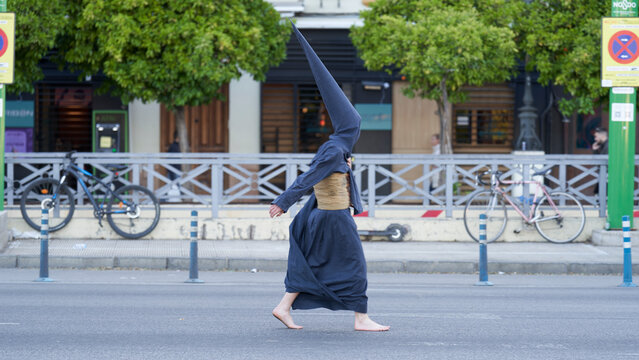 n this image, a Nazarene clad in black, including the capirote and esparto belt, walks alone down an empty street after completing his penance. The stillness of the scene accentuates the intensity of 