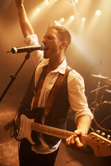 Night, singer and guitar with man on stage for music, performance and rock show. Event, spotlight...
