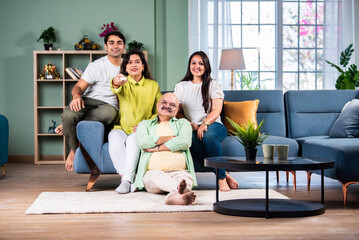Indian family of four sitting on couch watching TV, operating with remote control