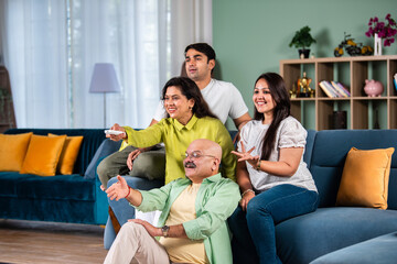 Indian family of four sitting on couch watching TV, operating with remote control