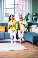Obraz premium Indian Cheerful old couple having coffee at home while sitting on sofa or staircase