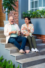Obraz premium Indian Cheerful old couple having coffee at home while sitting on sofa or staircase