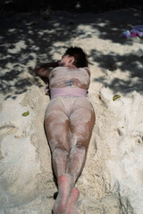 A woman with a short haircut lies on the sand on the beach.