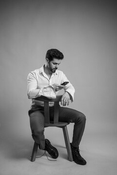 Young Man Sitting On A Chair While Checking His Smartphone