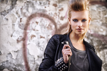 Woman, portrait and confident in edgy fashion with punk rock hairstyle, biker and cool in funky clothes by graffiti wall. Young model, face and leather jacket in urban town with trendy by street art