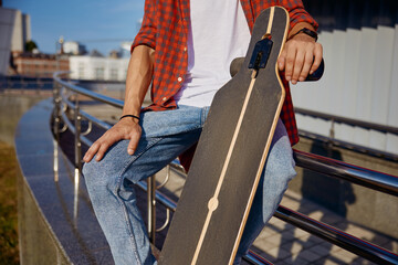 Closeup man holding skateboard in hand while sitting on steel railing