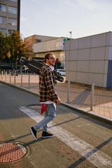 Fototapeta premium Young hipster man wearing casual attire walking with skateboard