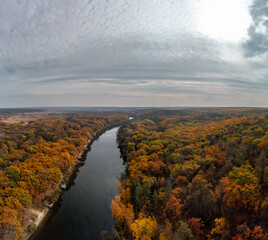 Autumn aerial river valley with colorful forest. Flying above autumnal vibrant trees near rural riverside in Ukraine