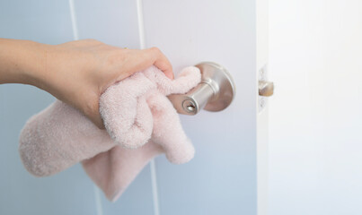 Closeup of woman's hands using a sanitizer and a wet towel for desinfection of the doors knob.