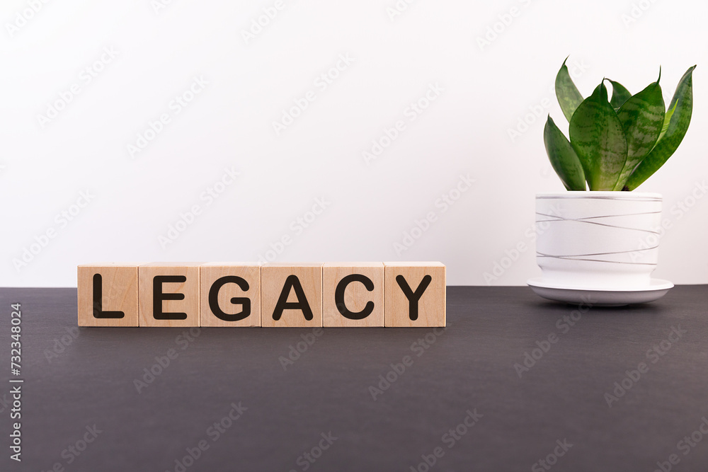 Fototapete legacy word on wooden cubes on a dark table with a flower and a light background