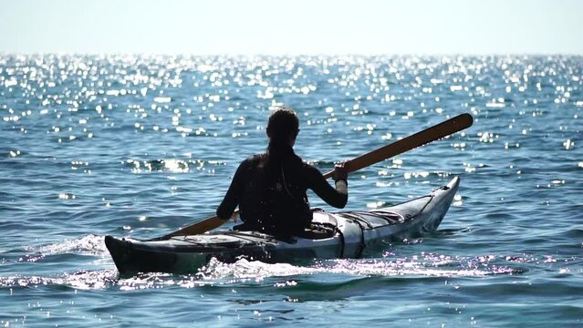 Woman sea kayak. Happy smiling woman in kayak on ocean, paddling with wooden oar. Calm sea water and horizon in background. Active lifestyle at sea. Summer vacation.
