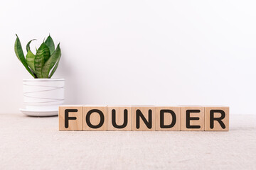 Founder word written on wooden cubes on a light table with a flower and a light background