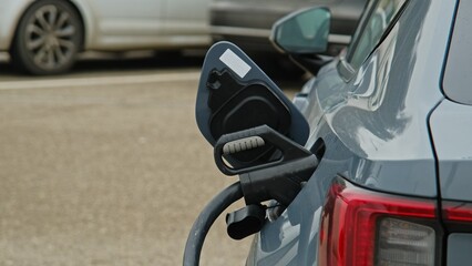 Electric Car with Plug In Charger Reacharging Battery on Outdoor Parking Lot 