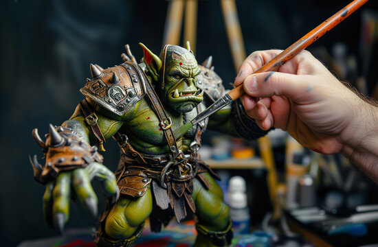 Close-up shot of a person's hand holding a paint brush, painting a large finely crafted miniature fantasy green ogre
