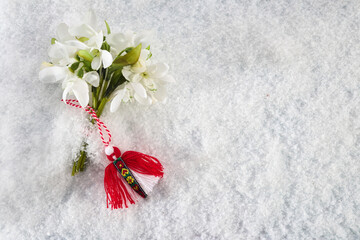 Fototapeta na wymiar Snowdrops flowers with a red and white martenitsa on a snow background. Martisor and Baba Marta.