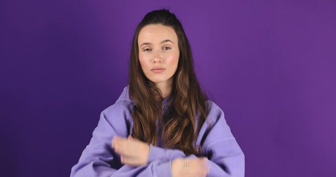 Brunette woman making hands stop action sign. Calm frustrated woman showing crossed arms in x gesture sign and looks on camera. Forbidden gesture standing isolated purple background. Break The Bias.