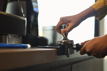 Cropped shot of barista hand tamping freshly ground coffee beans in a portafilter