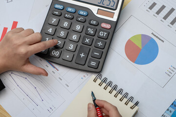 Liczyć na kalkulatorze, na biurku leżą dane finansowe, dokumenty z wykresami i tabelami kosztowymi